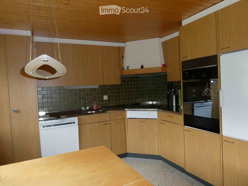 Modern kitchen with wooden cabinets, stainless steel appliances, and a central island table.