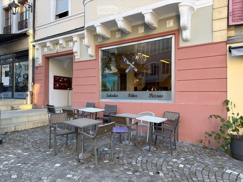 Outdoor seating area with tables and chairs in front of a restaurant named "Le Camillo Pizzeria" with a pink and cream facade.