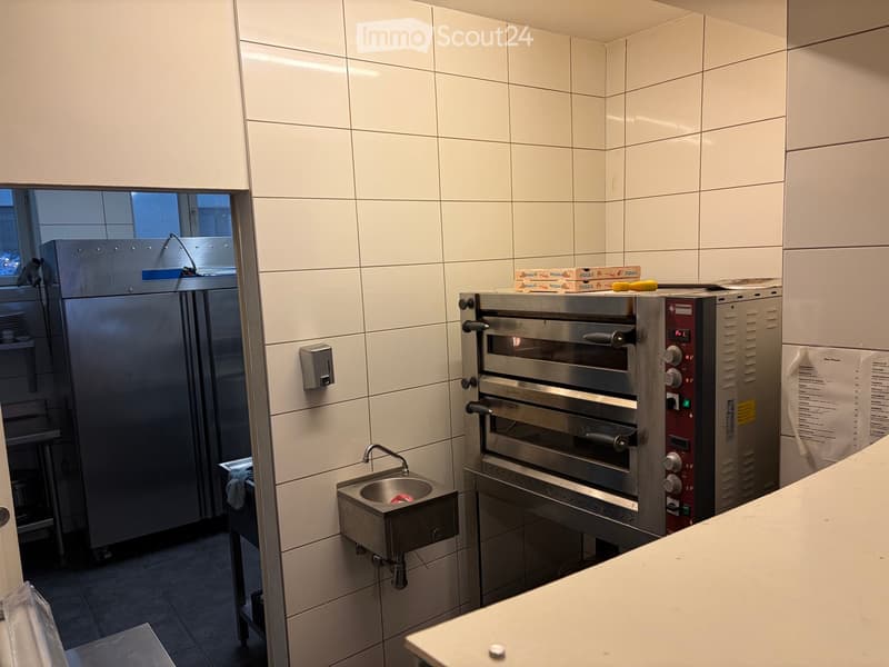 Commercial kitchen with stainless steel oven, refrigerator, sink, and counter.