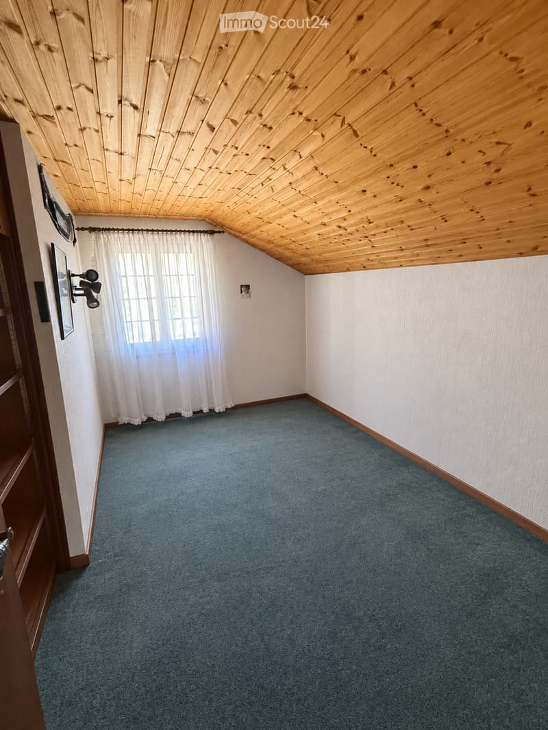 Empty room with blue carpet, white walls, wooden ceiling, and a window with white curtains.