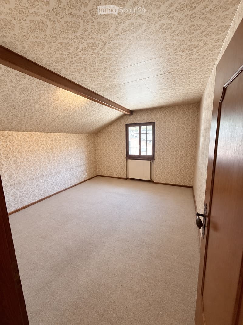 Empty room with beige carpet, patterned wallpaper, wooden trim, and a small window with a radiator below it.