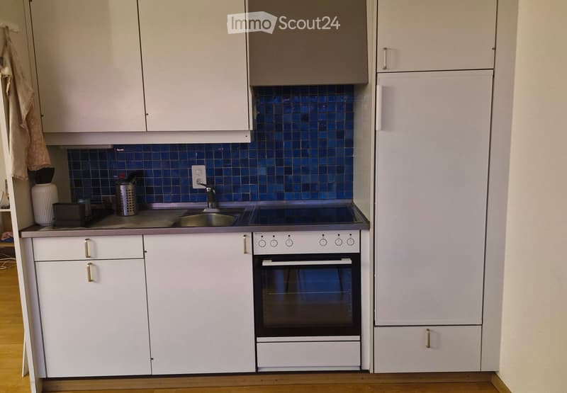 Modern kitchen with white cabinets, stainless steel sink, oven, and blue tiled backsplash.