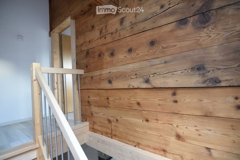 Wooden wall with a modern staircase featuring a white wooden handrail and metal balusters, leading to an upper level.
