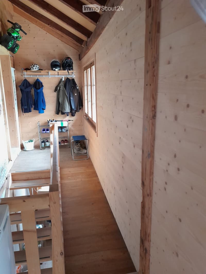 Wooden hallway with slanted ceiling, coat rack, storage shelves, and small window letting in natural light.