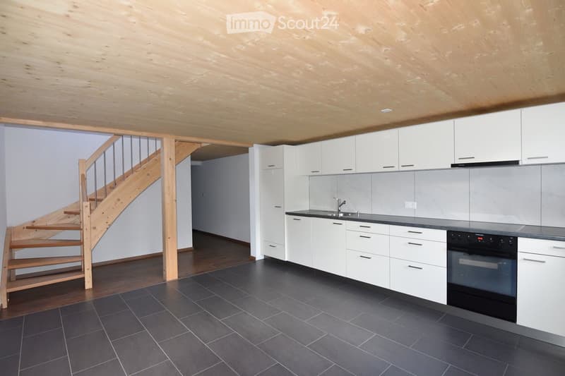 Modern kitchen with white cabinets, dark countertops, and a black tiled floor. Features a wooden staircase leading upwards.