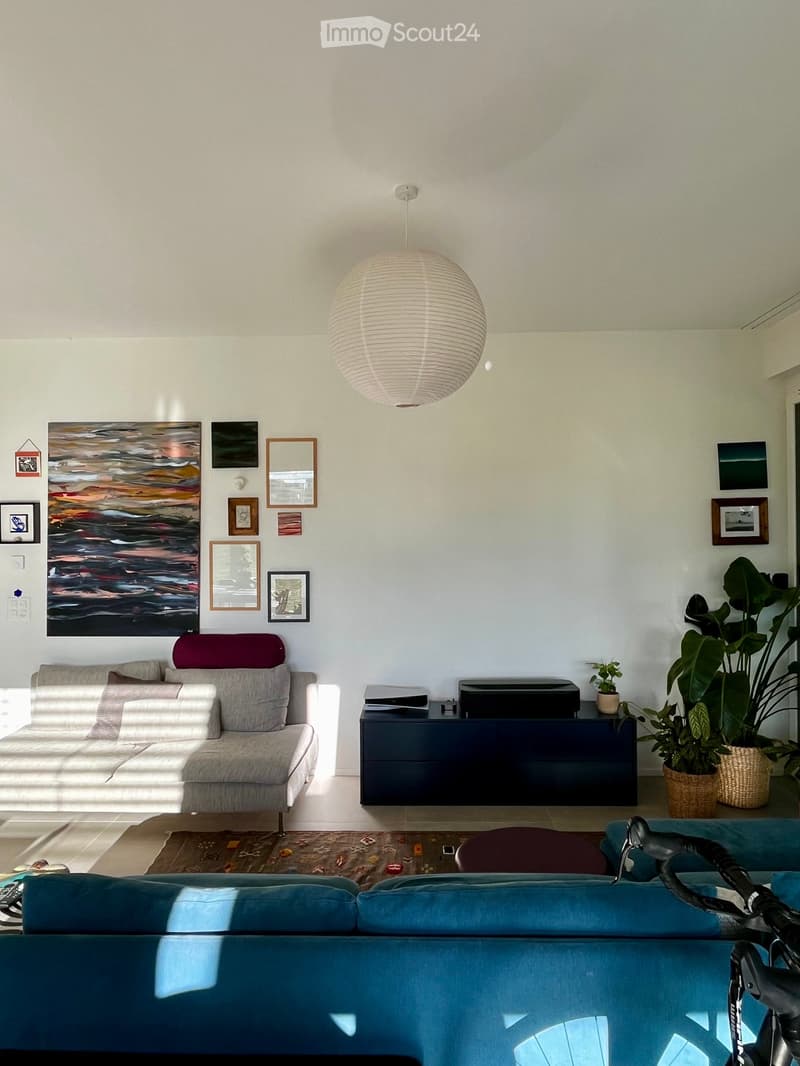 Modern living room with white walls, grey sofa, pendant light, coffee table, and framed artwork.