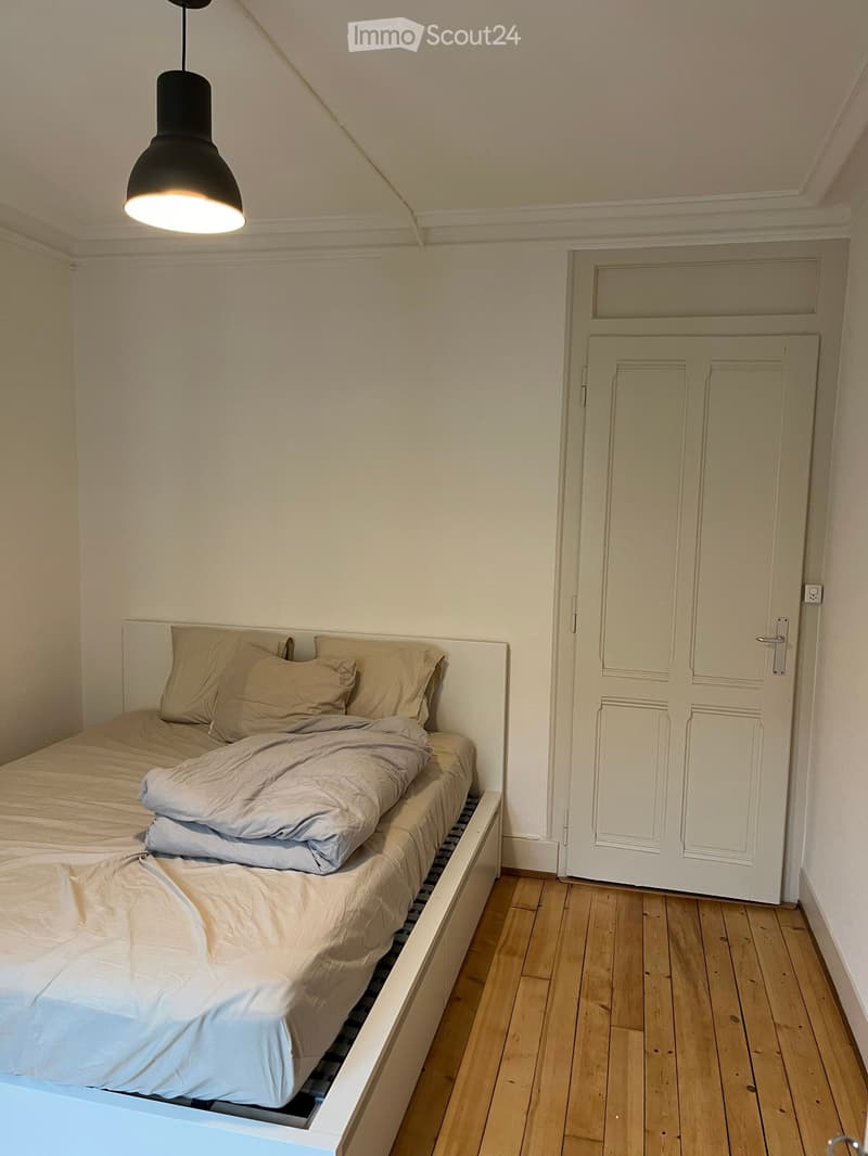 Cozy bedroom with a single bed, beige bedding, wooden floor, and a white door.