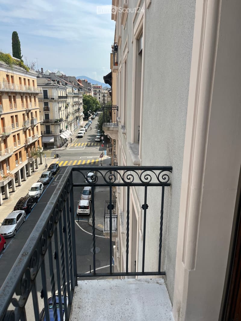Balcony overlooking a city street with parked cars, buildings, and a distant mountain view.