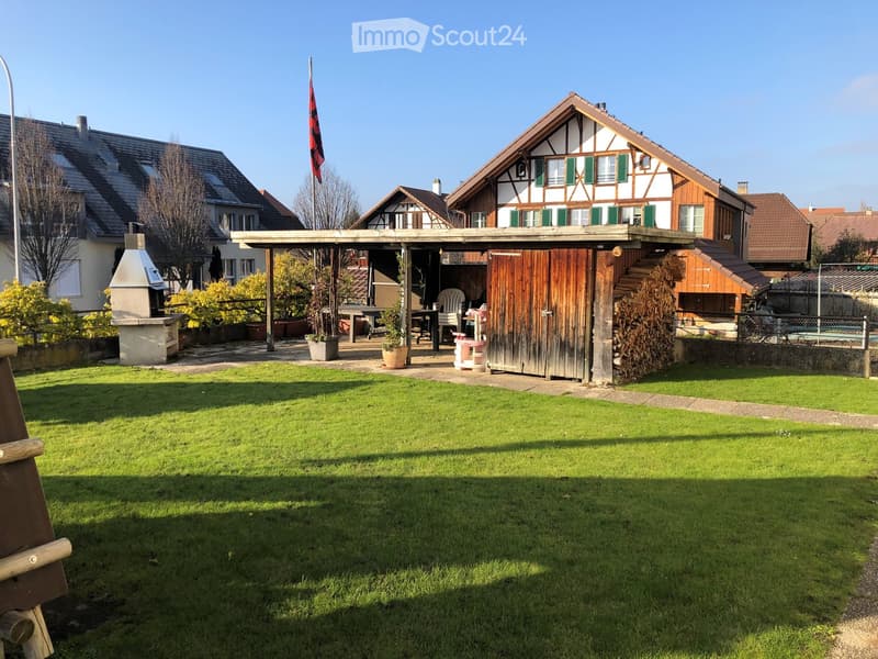 Well-maintained garden with a wooden pergola, outdoor furniture, barbecue, and a traditional half-timbered house in the background.