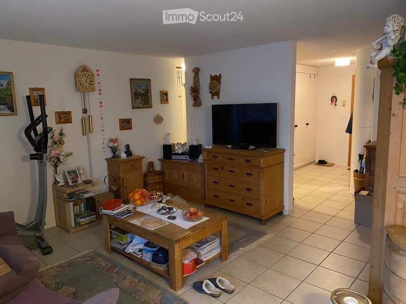 A cozy living room with a wooden coffee table, sofa, television on a dresser, decorative clocks, picture frames, and a small exercise bike in the corner.