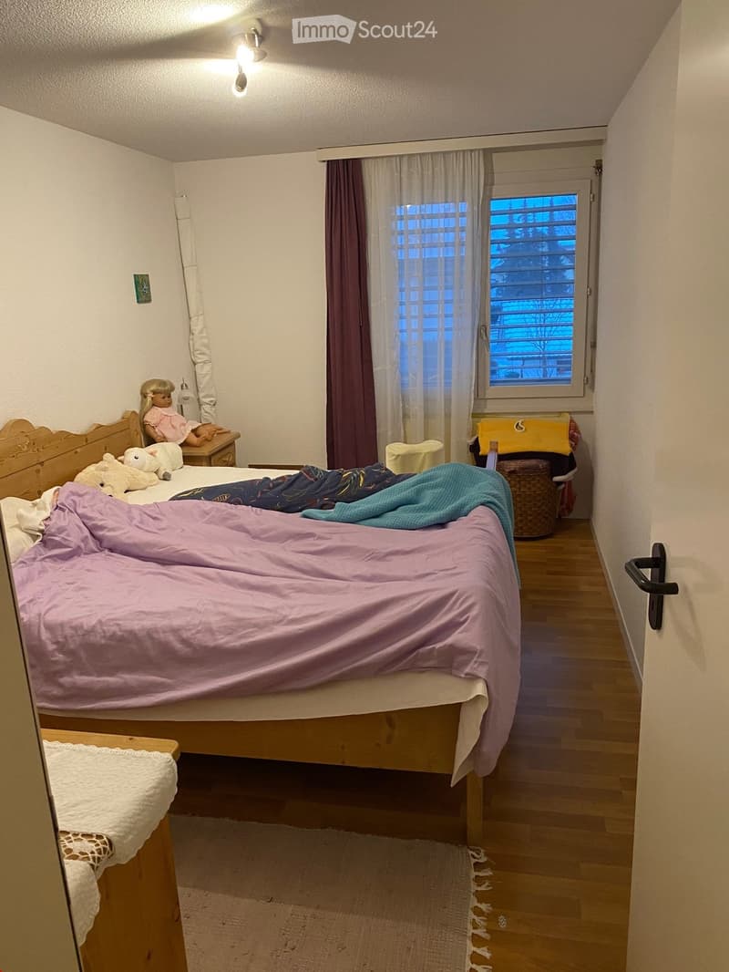Cozy bedroom with a wooden bed, nightstand, and various decorative items including a doll and pillows.