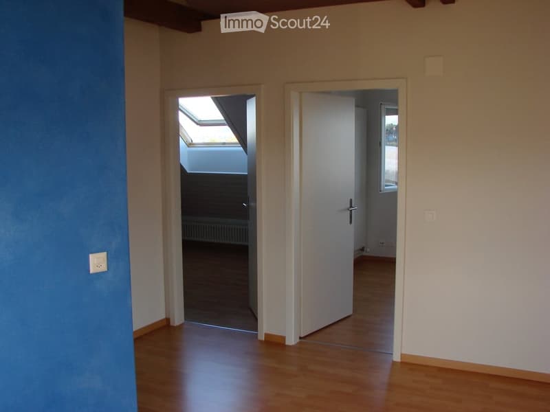 Empty room with wooden flooring, white walls, and two doors leading to other spaces. One door opens to a room with a window, and the other leads to a space with a skylight.