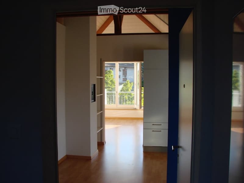 Bright hallway with wooden flooring, leading to a room with large windows and a balcony view.