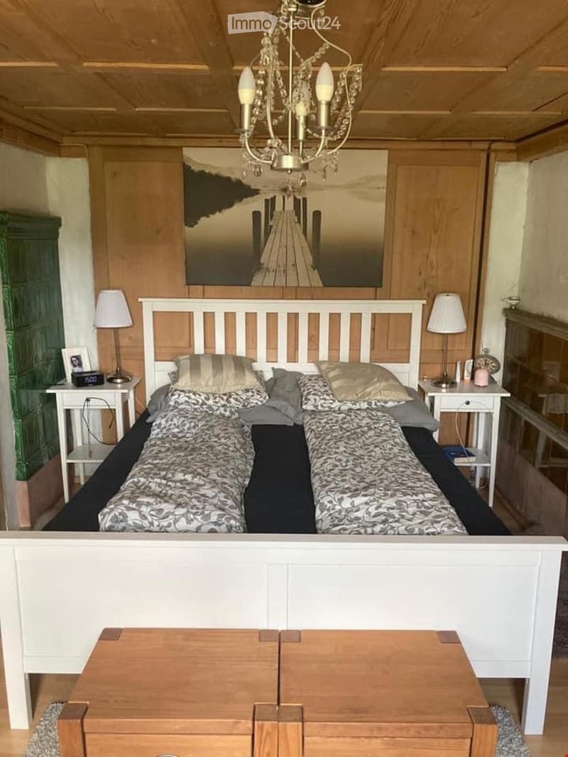 Cozy bedroom with a large double bed, two nightstands with lamps, a chandelier, and a scenic picture on the wall.