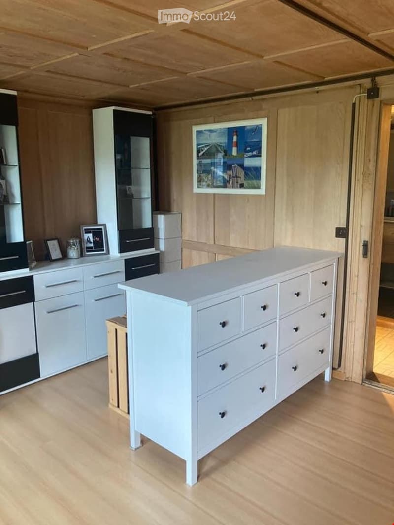 Modern kitchen with white cabinets, a large drawer unit, and a refrigerator. The room features wooden flooring and a wooden ceiling.