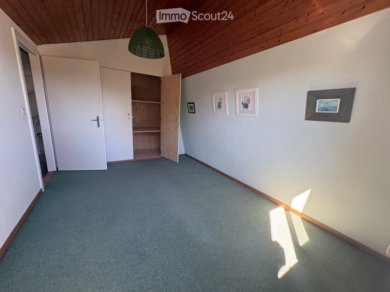 Empty room with light blue carpet, white walls, wooden ceiling, open closet, and framed pictures on the wall.