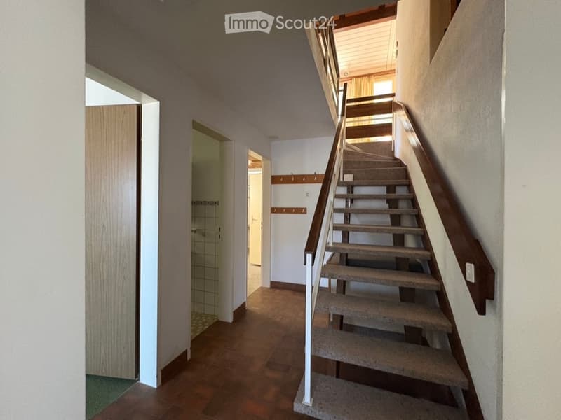 Hallway with wooden flooring, staircase leading to an upper level, coat rack, and open doors to adjacent rooms.