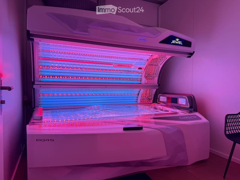 A modern tanning bed with multiple UV light panels, control panel, and a single chair nearby.