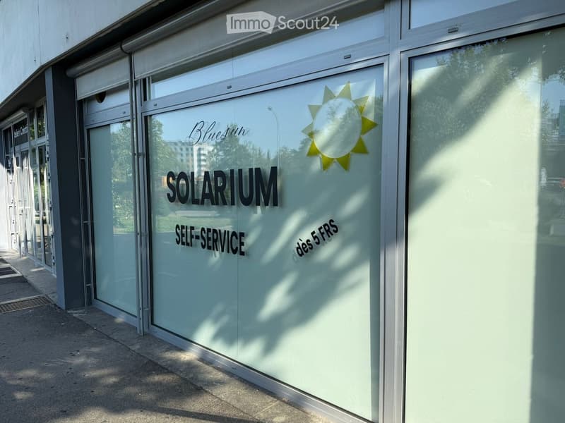 Exterior view of a building with a glass facade displaying the text "SOLARIUM" and "SELF-SERVICE" along with a sun graphic and the price "dés 5 FRS".