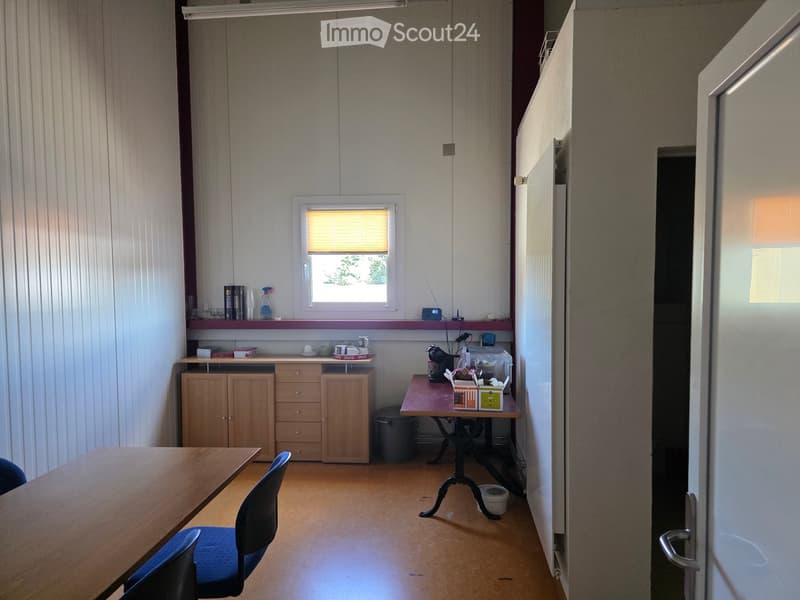 A small kitchen area with a wooden table, chairs, cabinets, and a refrigerator. There is a window with blinds and a small table with various items on it.