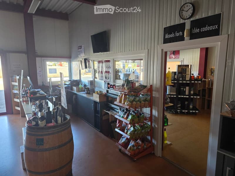 The image shows the interior of a small shop with a barrel, shelves filled with bottles, a screen, a clock, a table, a chair, a cash register, and a sign that reads "Alcools forts Idée cadeaux".
