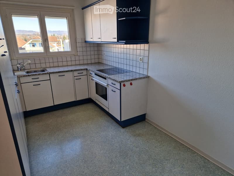 Modern kitchen with white cabinets, granite countertop, sink, and built-in oven. The space is clean and well-lit with large windows offering a view of the landscape.