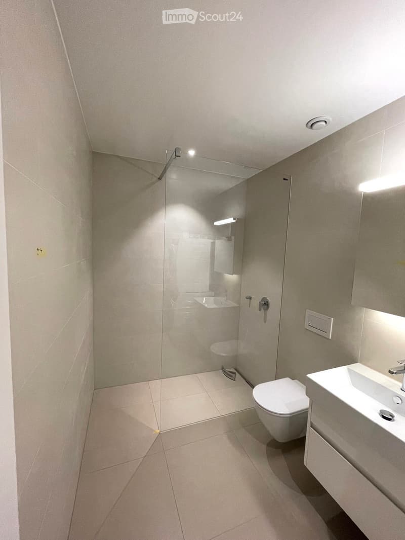 Modern bathroom with a white toilet, sink, and glass shower enclosure. Light-colored tiles and sleek fixtures.