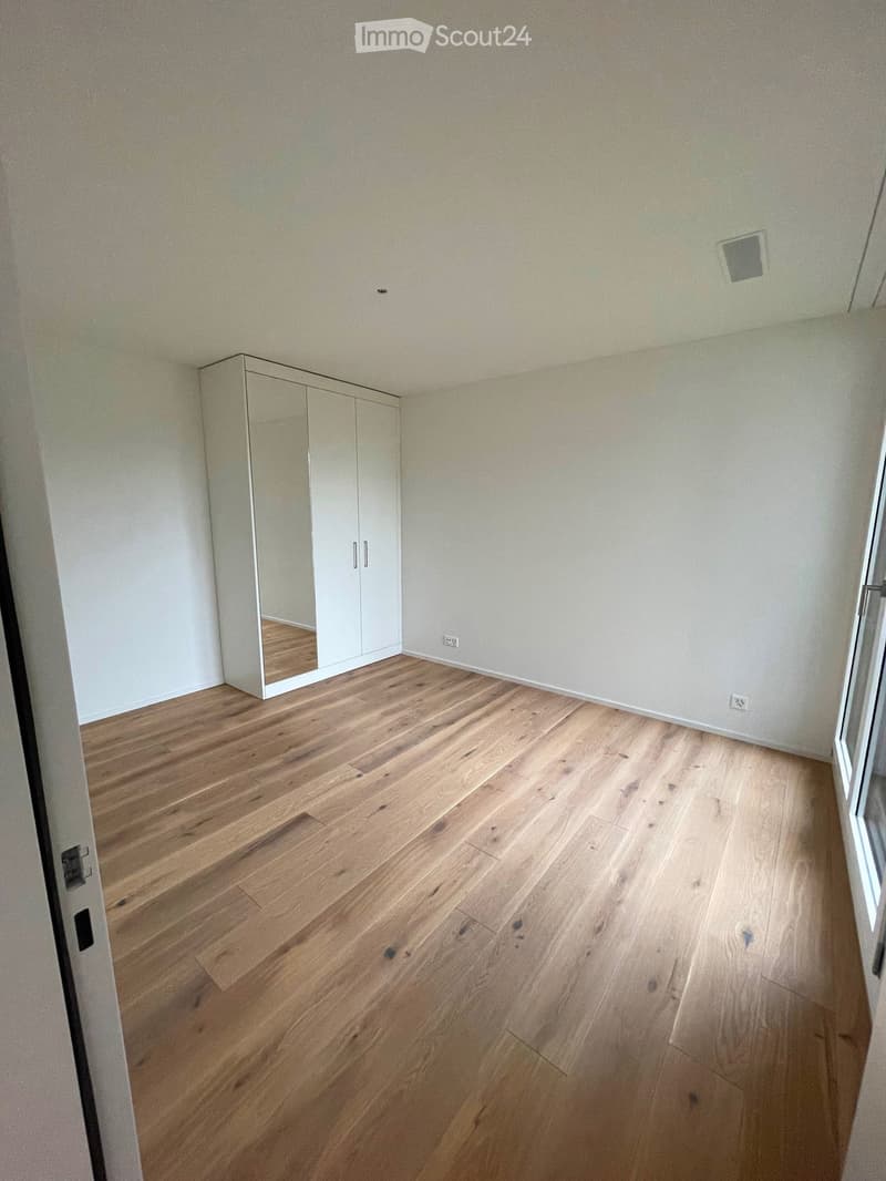 Empty room with light wooden flooring and white walls, featuring a built-in wardrobe with mirrored doors on one side.