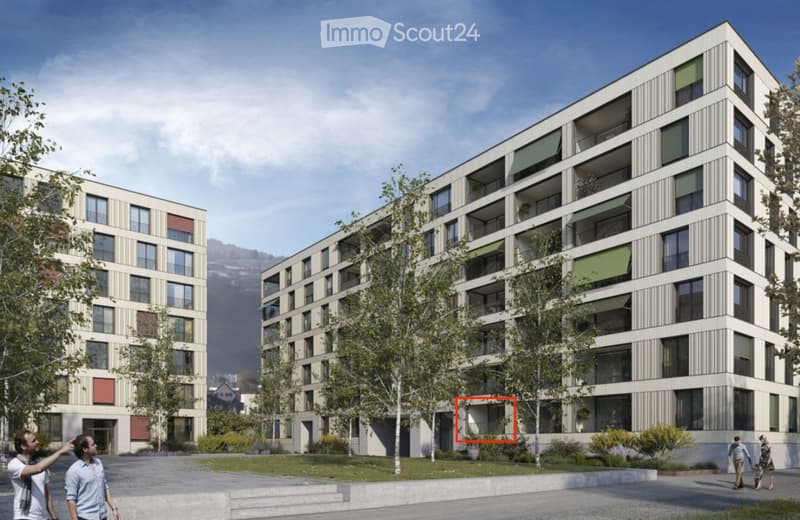 Modern multi-story residential building with balconies and green awnings, surrounded by trees and a paved area.