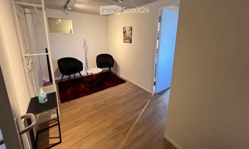 small room with wooden floor, two black chairs, small table, red rug, white walls, mirror, open door