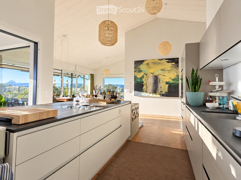 Modern kitchen with white cabinets, dark countertops, pendant lights, and a view of the outdoors.