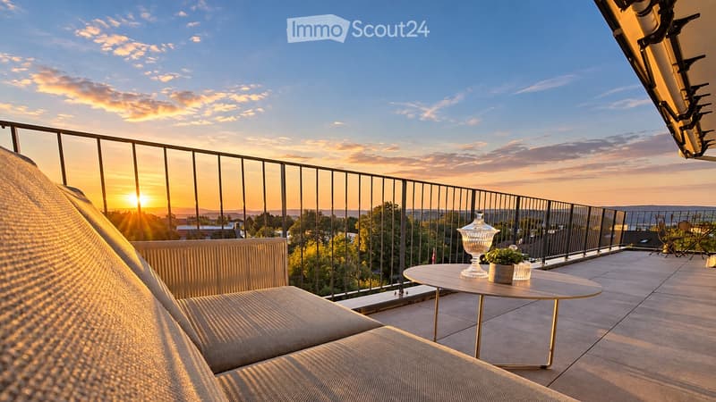 A modern balcony with a sofa, small round table, and chairs, overlooking a scenic sunset view.