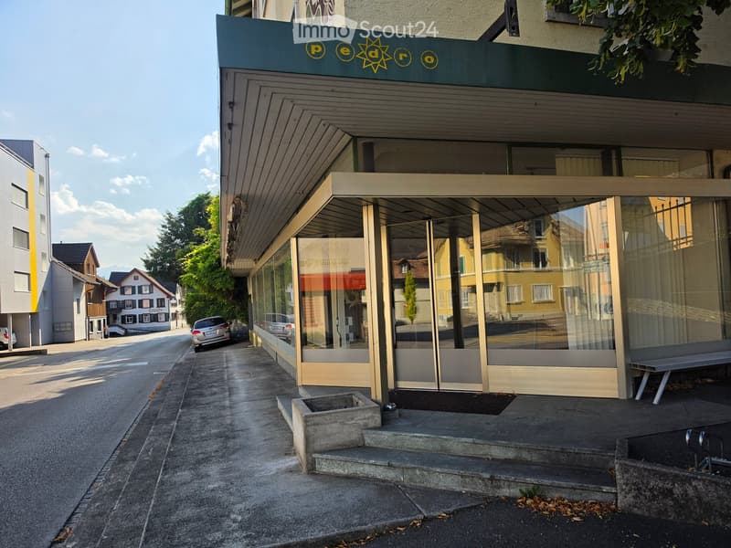 Modern building facade with large glass windows and a covered entrance, featuring a sign reading "pe dro" above the entrance.
