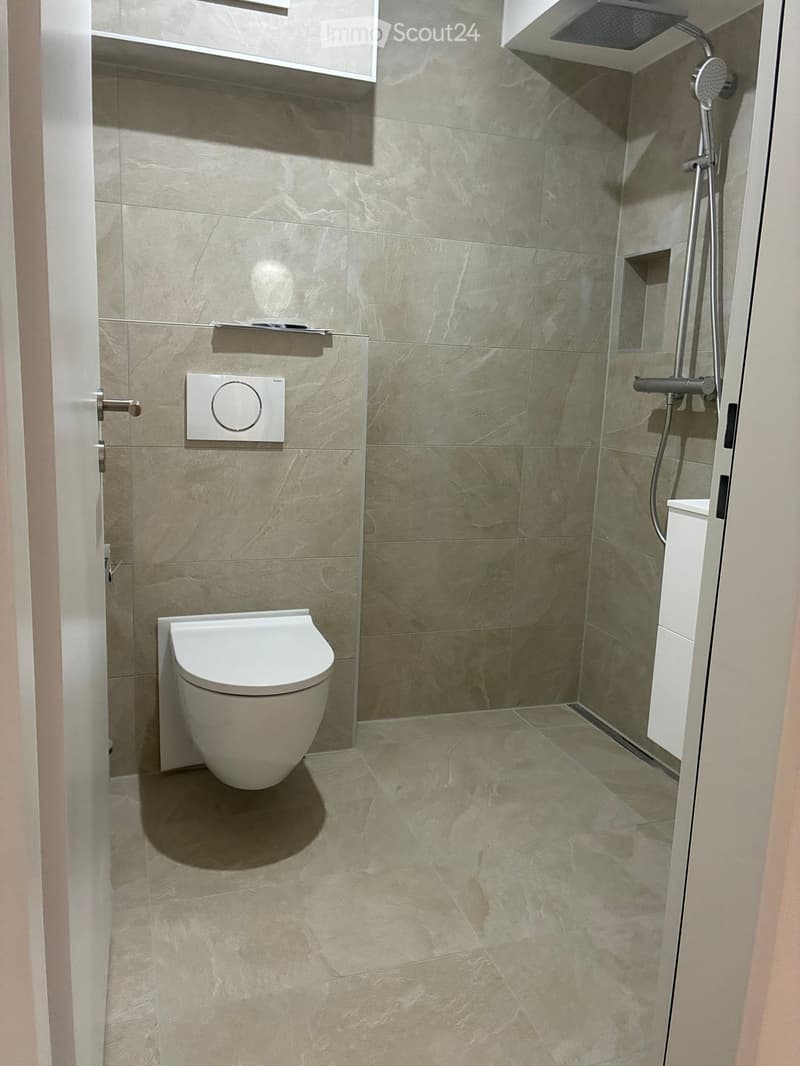 Modern bathroom with marble tiles, a toilet, a shower area with a handheld showerhead, and a sleek faucet.
