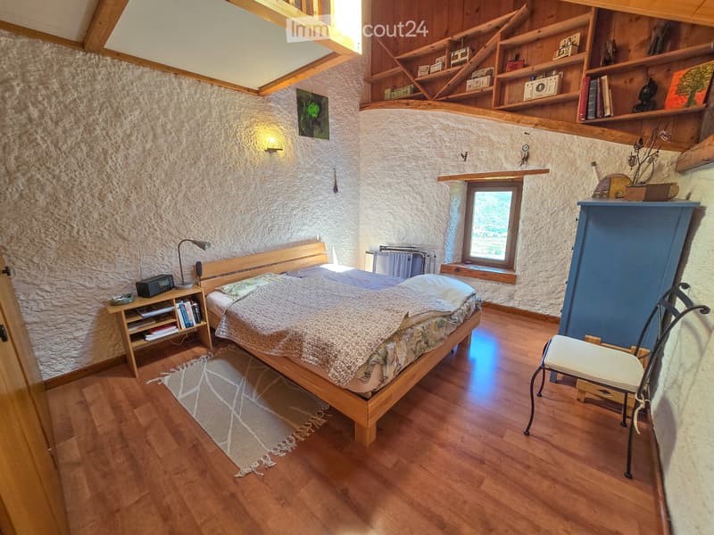 Cozy bedroom with wooden bed, nightstand, chair, shelves, and a window offering a view.