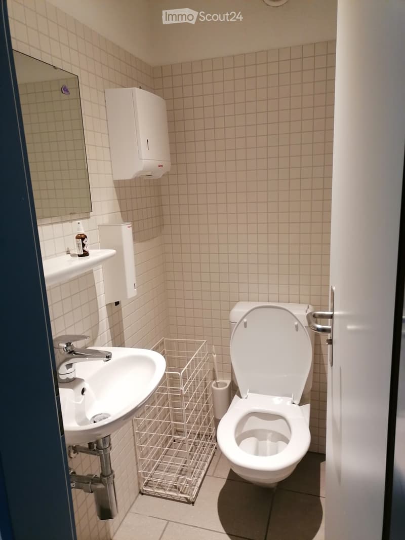 A small bathroom with a toilet, sink, mirror, and a towel rack. The walls are tiled, and the floor is tiled as well.