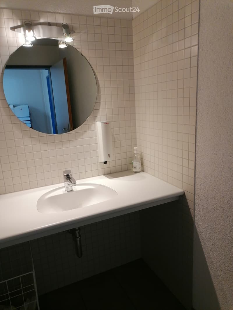 Modern bathroom with a white sink, chrome faucet, round mirror with built-in lighting, and a soap dispenser on the counter.