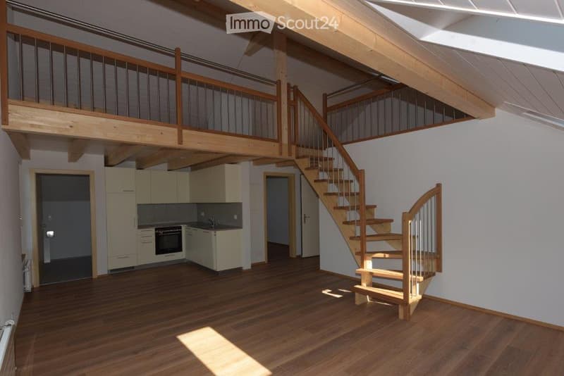 Open-plan space with wooden flooring, a staircase leading to an upper level, and a small kitchen area with cabinets and appliances.