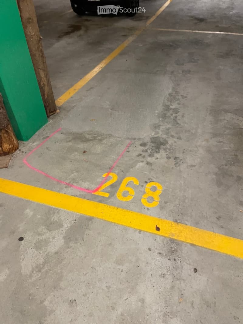 Parking space marked with yellow lines and number 268, concrete floor, green barrier on the left side.