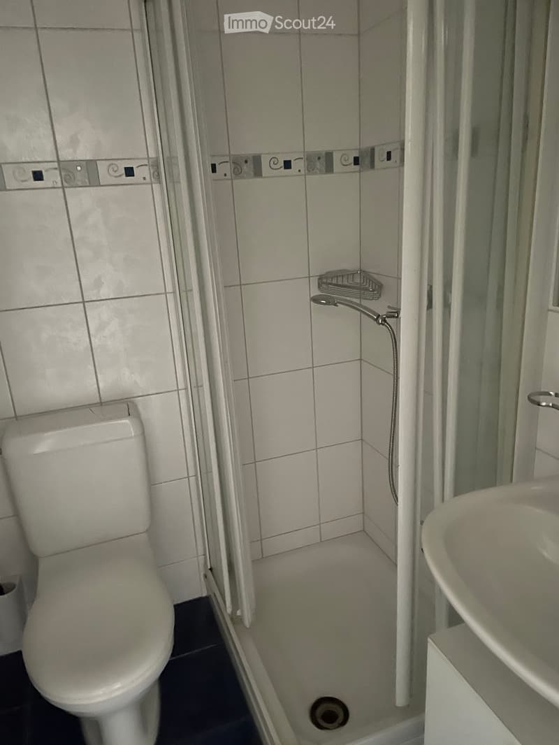 A small bathroom with a toilet, a sink, and a shower area with a glass enclosure. The walls are tiled with a decorative border near the top.