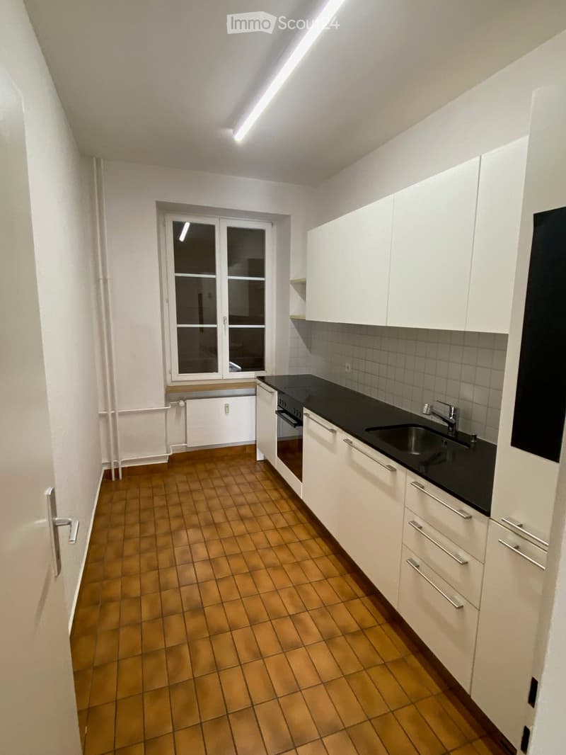 Modern kitchen with white cabinets, black countertops, and a stainless steel sink. The floor is tiled in a warm, earthy tone.