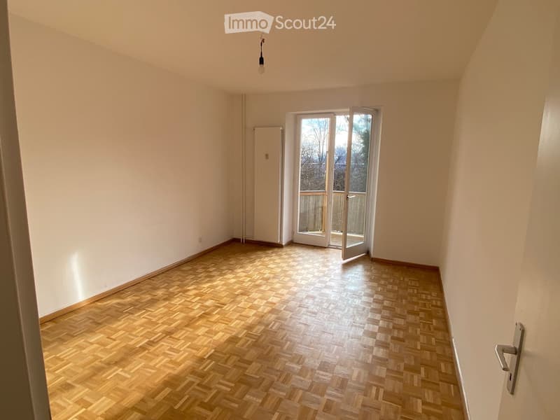 Empty room with wooden herringbone flooring, white walls, and a large sliding glass door leading to a balcony.