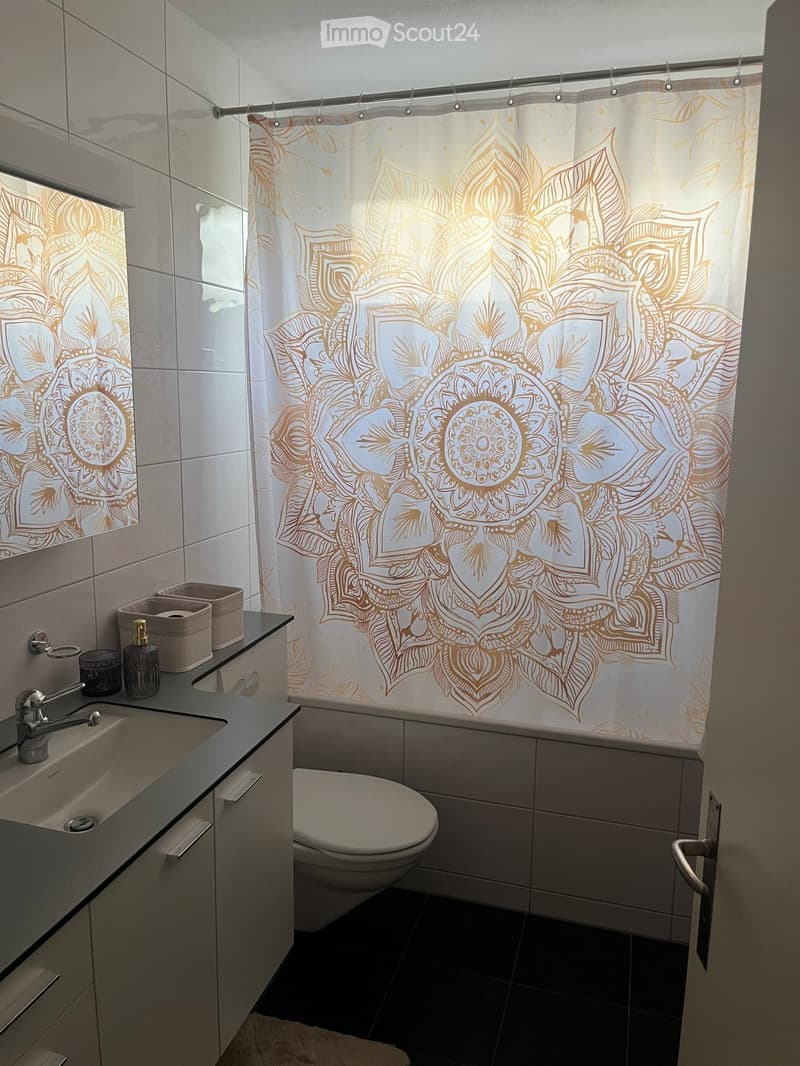 Modern bathroom with a white toilet, black countertop sink, and decorative shower curtain with a mandala design.