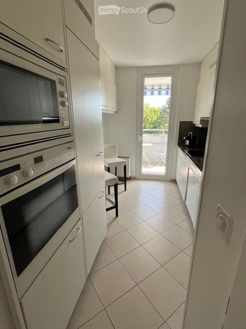 Modern kitchen with white cabinets, stainless steel appliances, tiled floor, and access to a balcony.