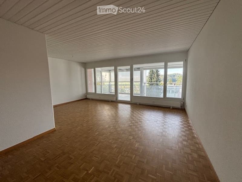 Completely empty room with wooden flooring and large windows, no furniture or equipment.
