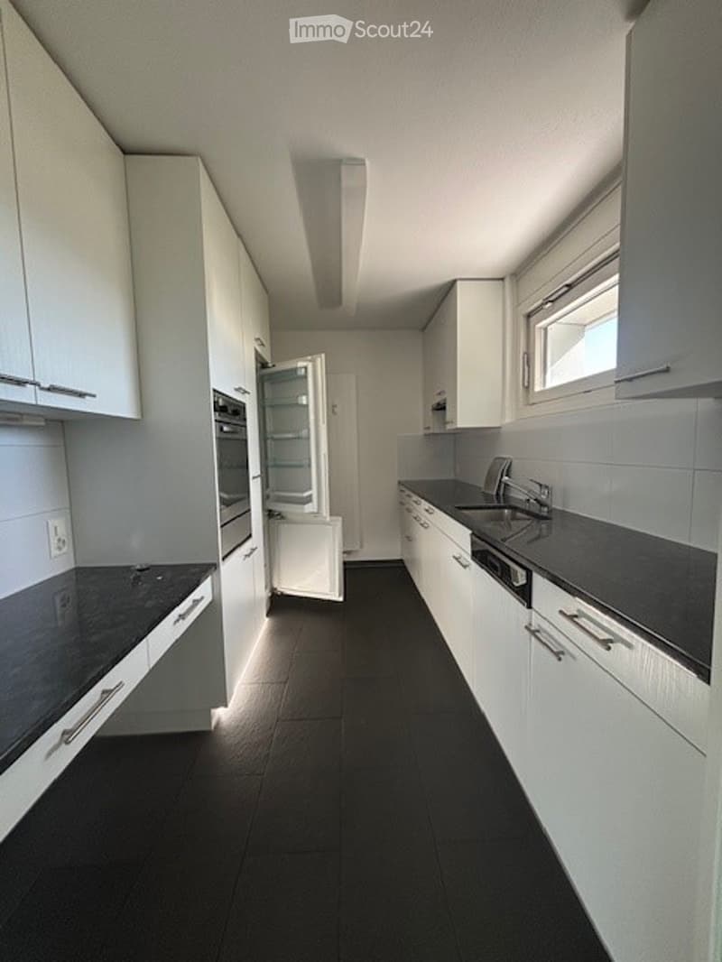 Modern kitchen with white cabinets, black countertops, and black tiled flooring. Features include a refrigerator, sink, and oven.