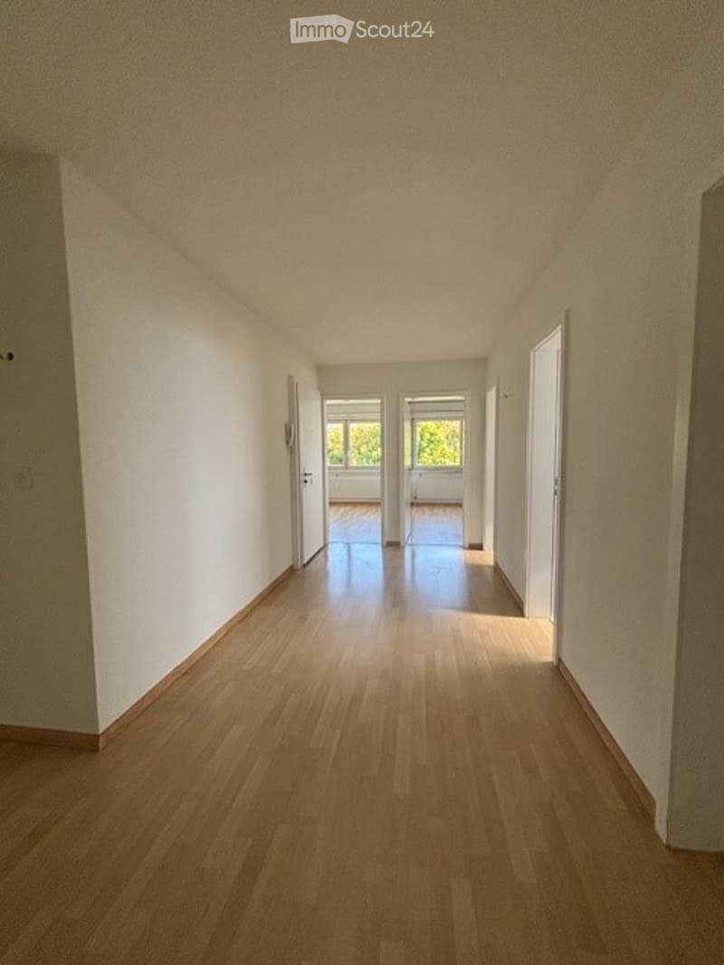 Empty hallway with wooden flooring and white walls, leading to two open doors at the end.
