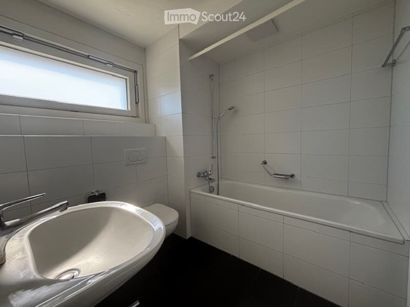 Modern bathroom with white tiled walls and black flooring, featuring a sink, toilet, and bathtub with a showerhead.