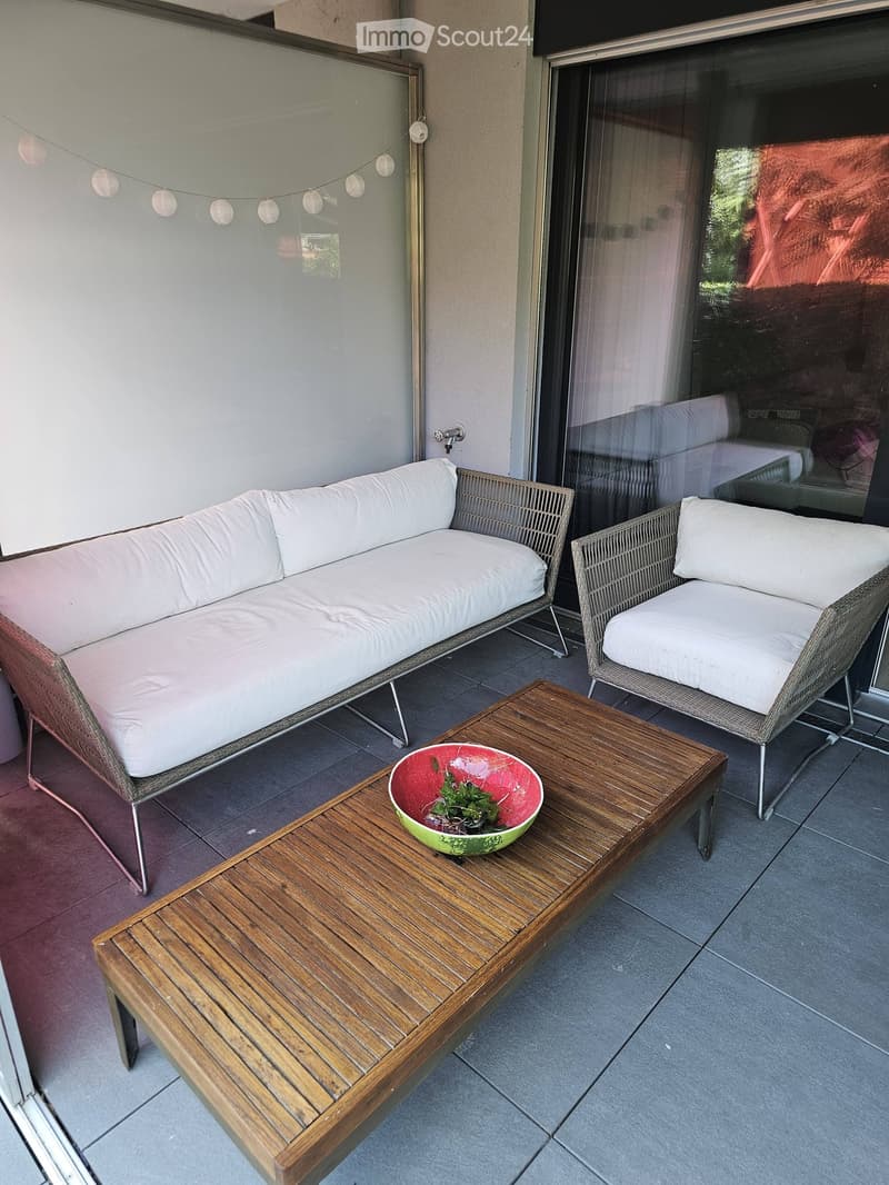 Balcony with a wooden coffee table, a red and green bowl with greenery, a white cushioned sofa, and a matching chair.
