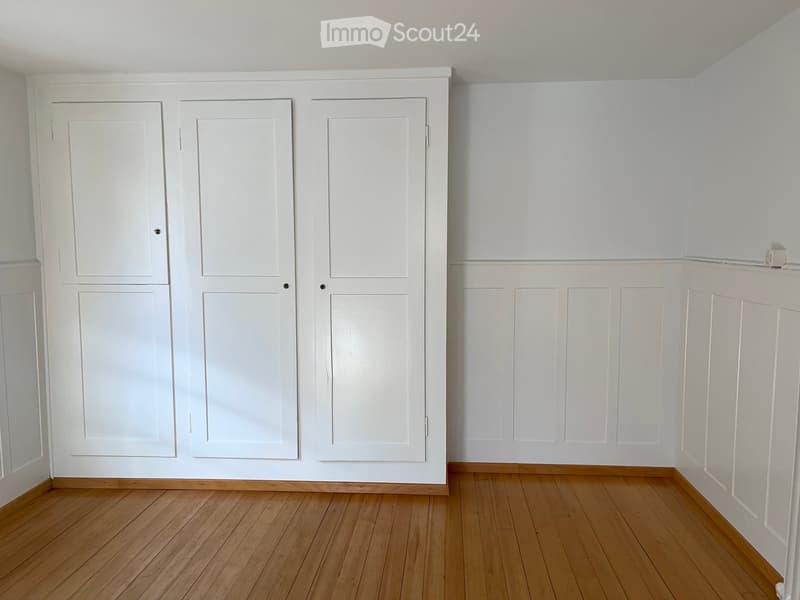 Empty room with white walls, wooden floor, and three white doors.
